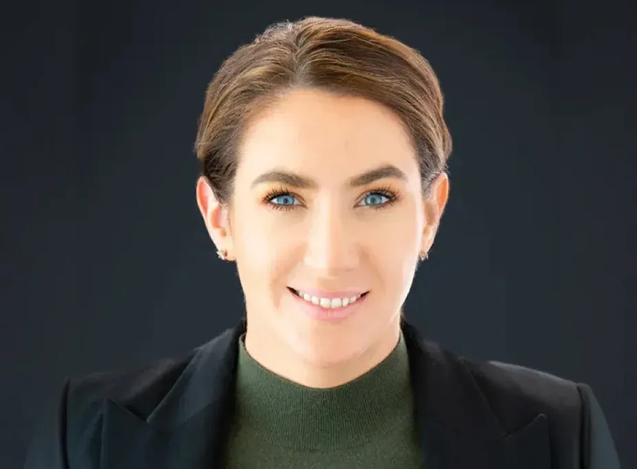 Smiling woman with short brown hair wearing a black blazer and green top.